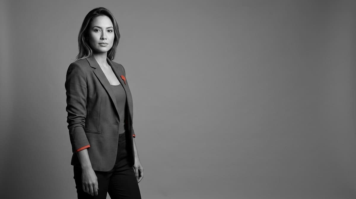 Mulher com blazer moderno sorrindo em um retrato de estúdio com fundo liso e neutro.