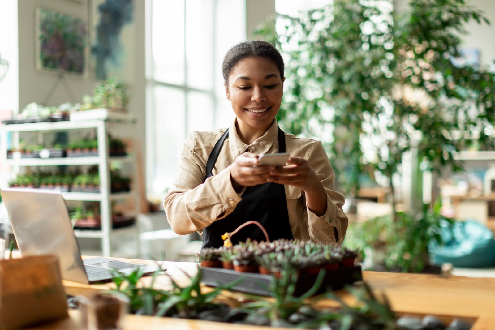 Dona de pequeno negócio sorrindo enquanto fotografa seus produtos com o celular para postar nas redes sociais
