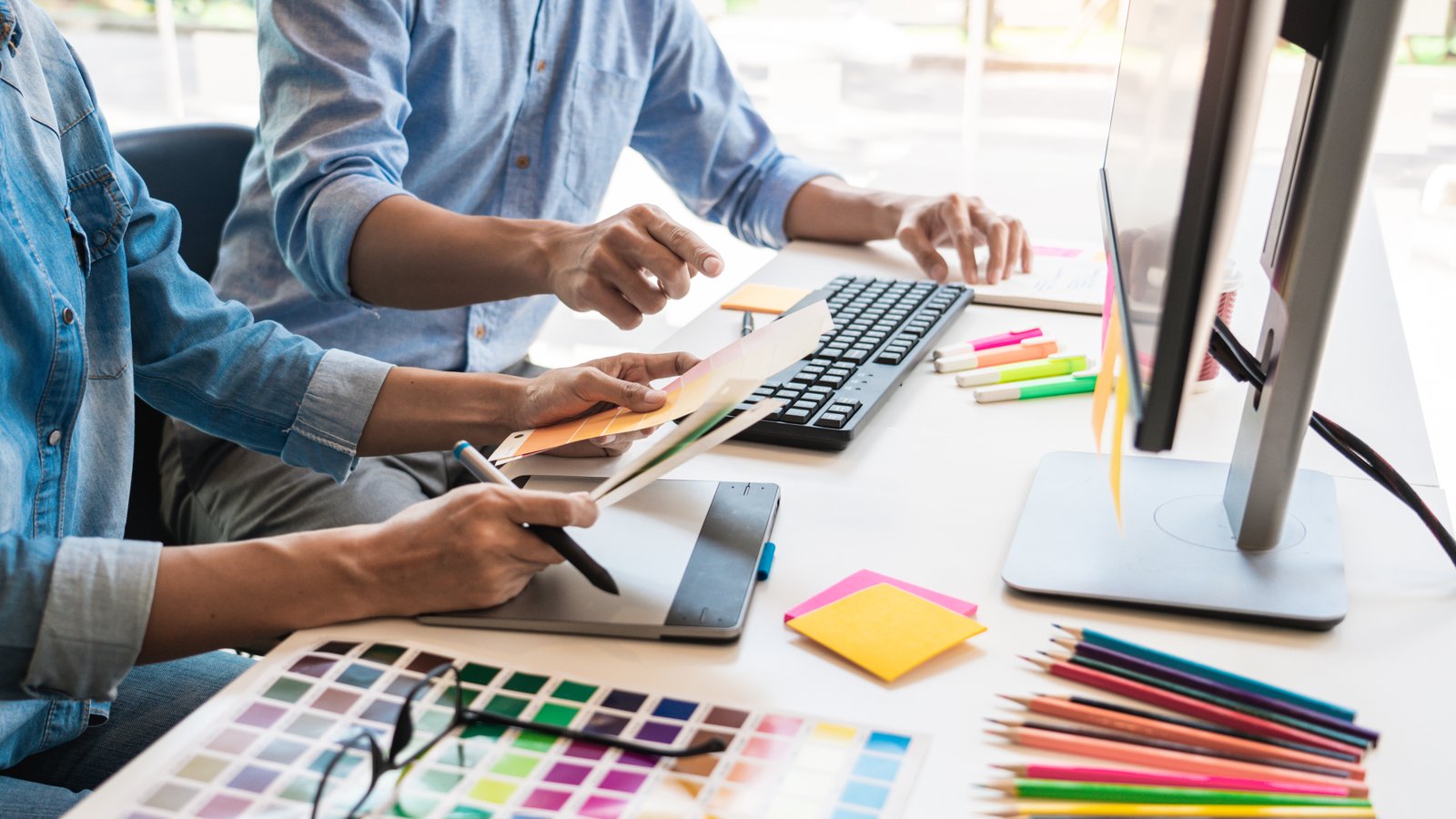 Duas pessoas trabalhando juntas em uma mesa, usando mesa digitalizadora e paleta de cores para planejar conteúdo visual